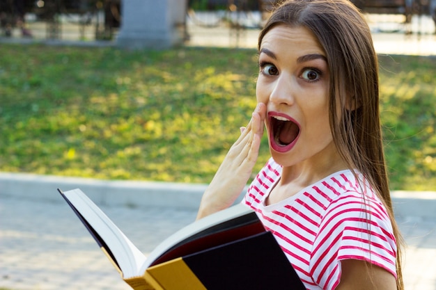 Niña sorprendida leyendo un libro afuera.