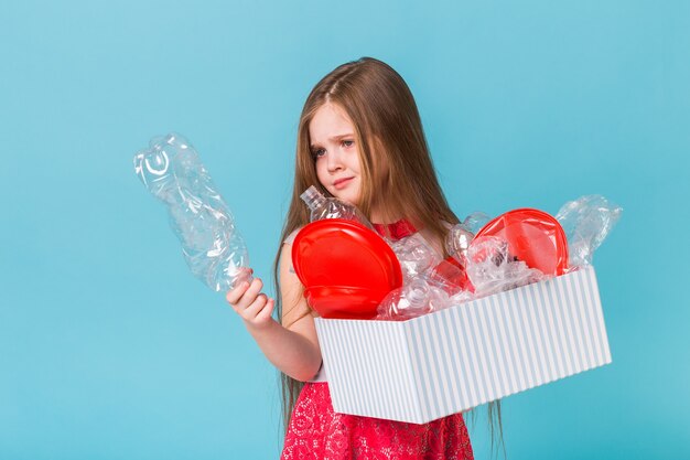 Niña sorprendida mira con los ojos abiertos y expresión preocupada sosteniendo la caja con basura