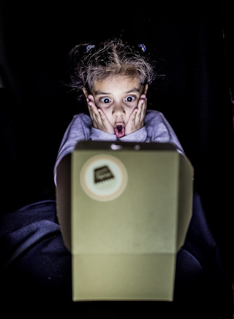 Foto niña sorprendida mirando la caja en el cuarto oscuro