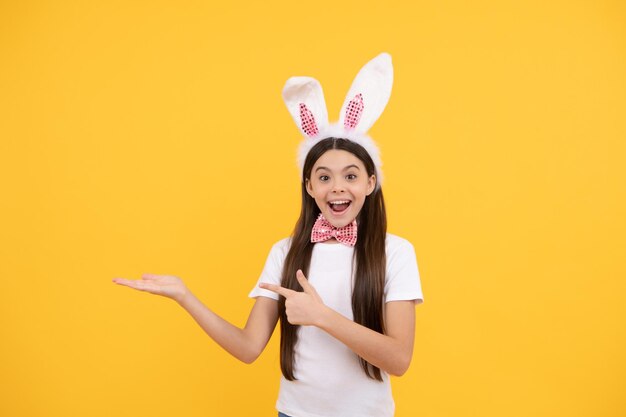 Niña sorprendida de pascua con orejas de conejo y pajarita que presenta el producto o las ventas de compras espacio de copia venta de pascua