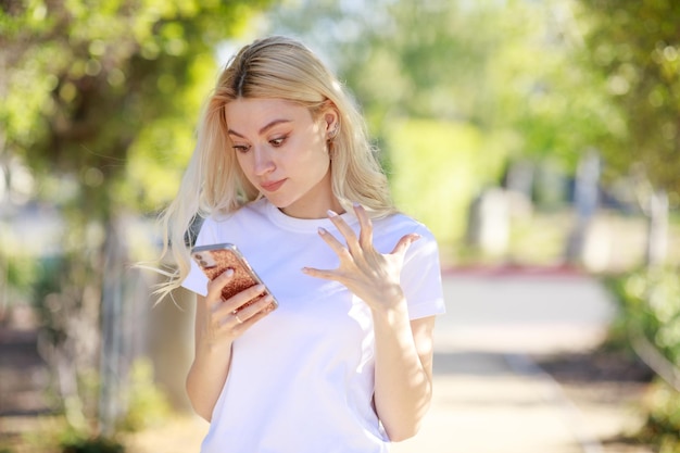 Niña sorprendida de pie en el parque y mirando su teléfono