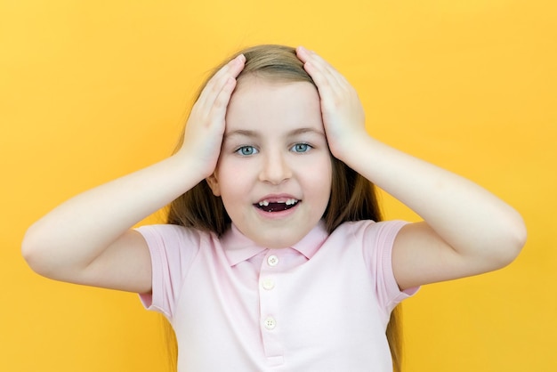 Niña sorprendida sosteniendo su cabeza con las manos, los dientes delanteros del niño se cayeron sobre un fondo amarillo