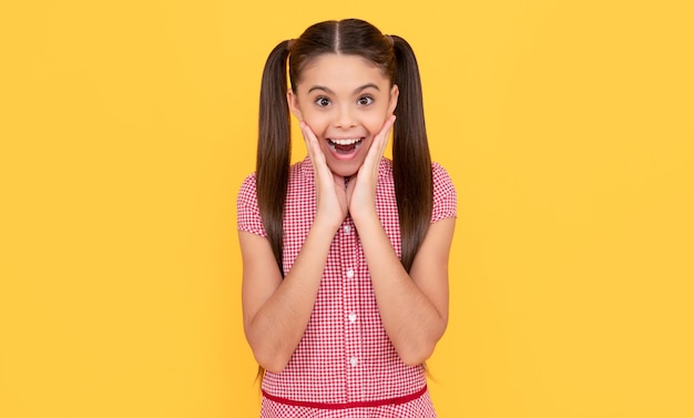 Foto niña sorprendida toca cara hermosa manteniendo la boca abierta con belleza de fondo amarillo sorpresa