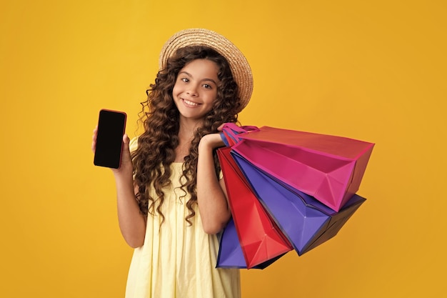 Niña sostenga una bolsa de compras y un teléfono móvil disfrutando de la venta aislada en un fondo amarillo Retrato de una adolescente lista para ir de compras