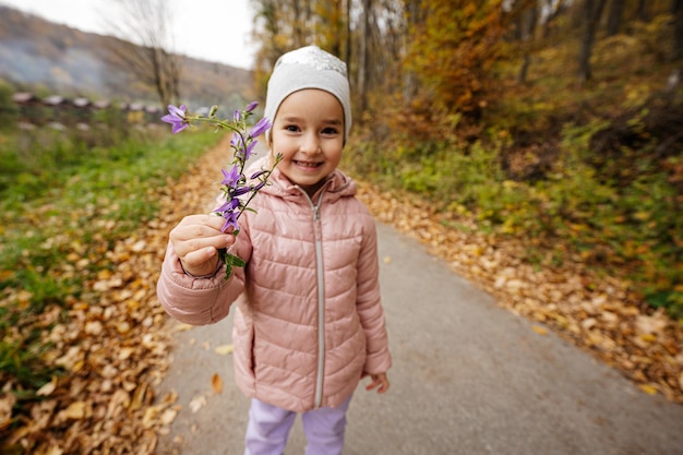 Niña sostenga en la mano Campanula campanas de flores moradas en el bosque de otoño