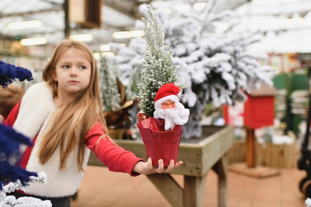 Niña sosteniendo un árbol de Navidad artificial con Santa Claus