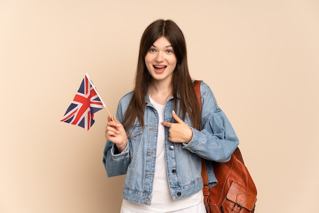 Niña sosteniendo una bandera del Reino Unido aislada en beige con expresión facial sorpresa