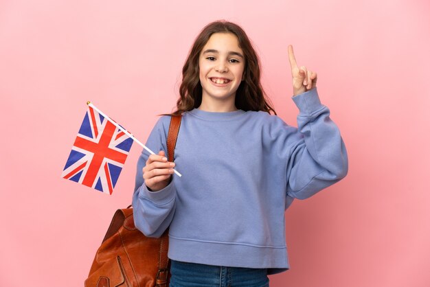 Niña sosteniendo una bandera de Reino Unido aislada sobre fondo rosa apuntando hacia una gran idea