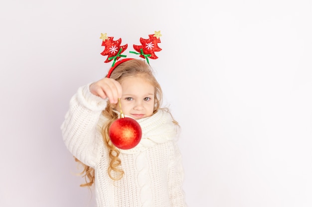 Niña sosteniendo una bola de Navidad roja sobre blanco