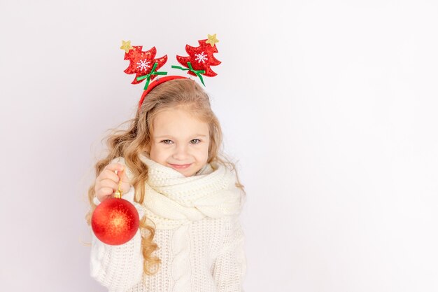 Niña sosteniendo una bola de Navidad roja sobre un fondo blanco aislado, espacio para texto