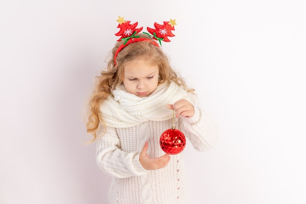 Niña sosteniendo una bola de Navidad roja sobre un fondo blanco aislado