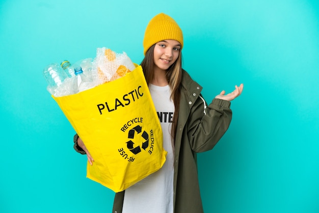 Niña sosteniendo una bolsa llena de botellas de plástico para reciclar sobre fondo azul aislado extendiendo las manos hacia el lado para invitar a venir