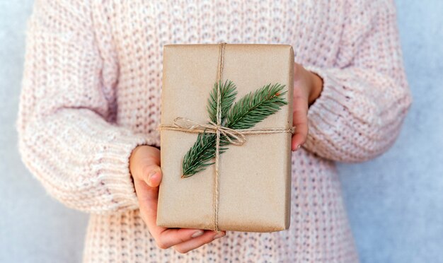 Una niña sosteniendo una caja de regalo Crhistmas de desperdicio cero envuelta en papel kraft y decorada con rama de abeto