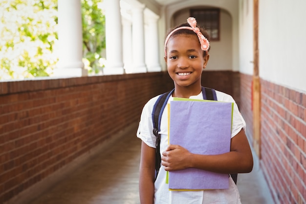 Niña sosteniendo carpetas en el pasillo de la escuela