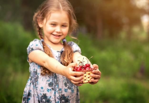 Niña sosteniendo una cesta de cerezas en la naturaleza en verano