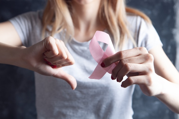 Niña sosteniendo una cinta rosa y mostrando el pulgar hacia abajo