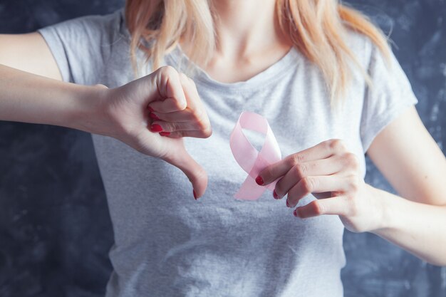 Niña sosteniendo una cinta rosa y mostrando el pulgar hacia abajo