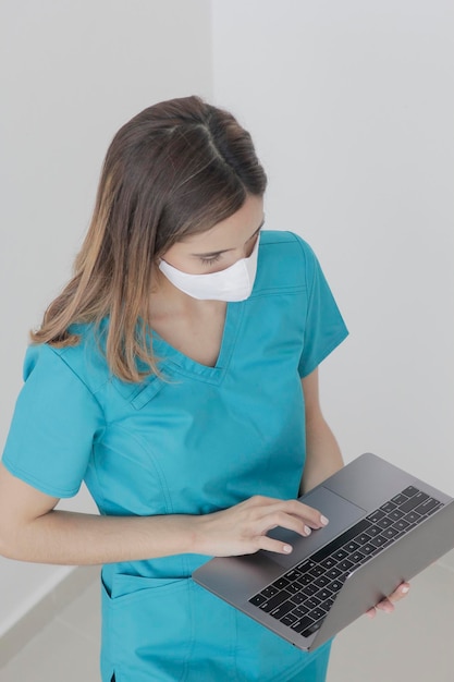 Niña sosteniendo una computadora portátil mientras trabaja en la enfermera del hospital con máscara