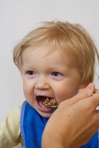 Niña sosteniendo una cuchara en sus brazos y comiendo una papilla