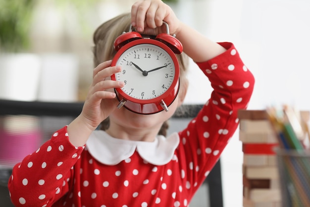 Niña sosteniendo un despertador rojo frente a su cara