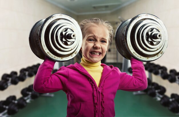 Niña sosteniendo dos mancuernas duras en el gimnasio