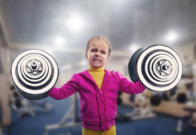 Niña sosteniendo dos pesadas pesas en el gimnasio