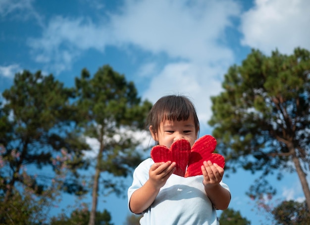 Niña sosteniendo formas de corazón contra los árboles