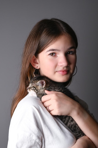 Niña sosteniendo un gato bebé dormido sobre fondo gris Hembra abrazando a su lindo gatito Adorable concepto de mascota doméstica