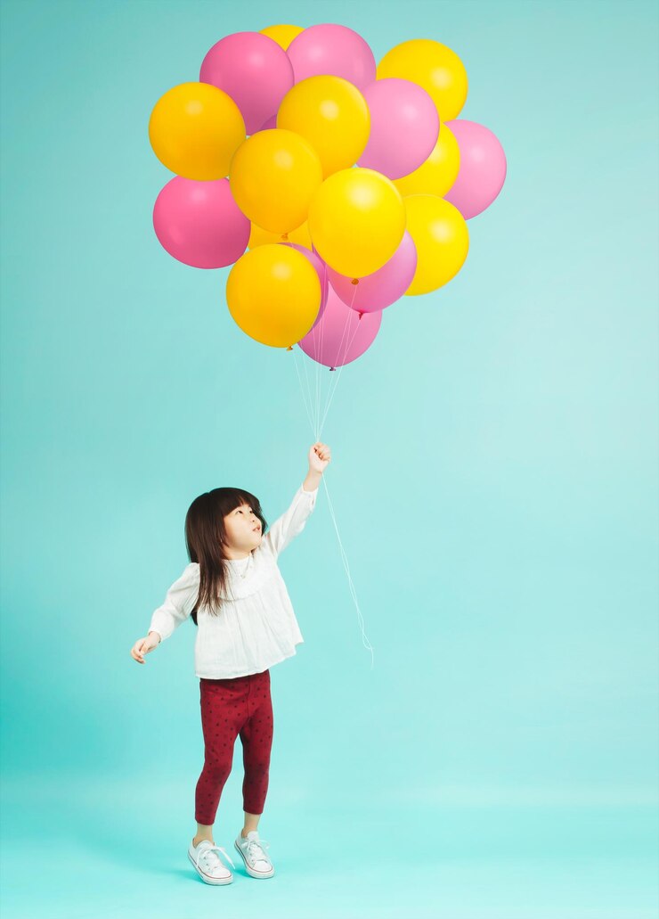 Niña sosteniendo globos de helio sobre fondo liso