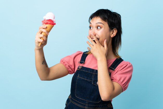 Niña sosteniendo un helado de cucurucho sobre azul aislado con sorpresa y expresión facial conmocionada