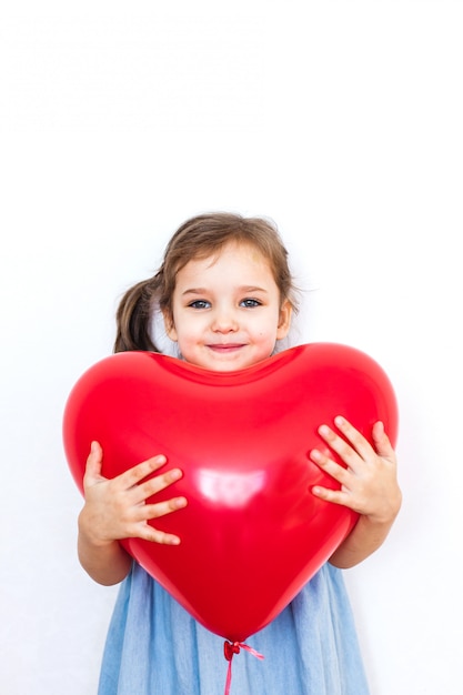 Niña sosteniendo un hermoso globo rojo en forma de corazón para un regalo para el día de San Valentín, los amantes, el día de San Valentín, la familia y el corazón