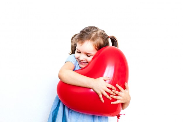 Niña sosteniendo un hermoso globo rojo en forma de corazón para un regalo para el día de San Valentín, los amantes, el día de San Valentín, la familia y el corazón