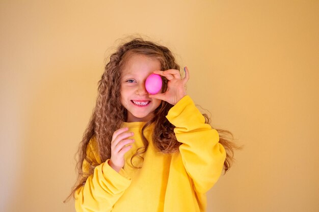 Una niña sosteniendo un huevo frente a un fondo amarillo.