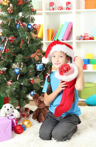 Niña sosteniendo un juguete cerca del árbol de Navidad