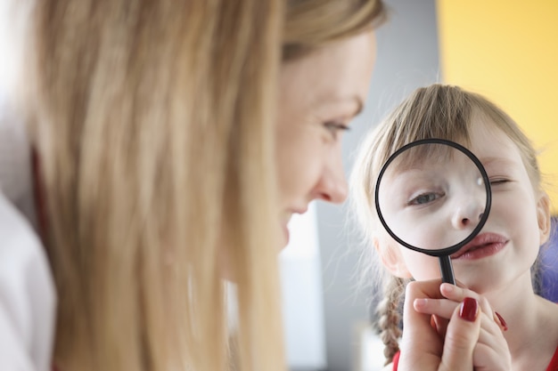 Niña sosteniendo lupa cerca del ojo junto a su madre médico preventivo anual