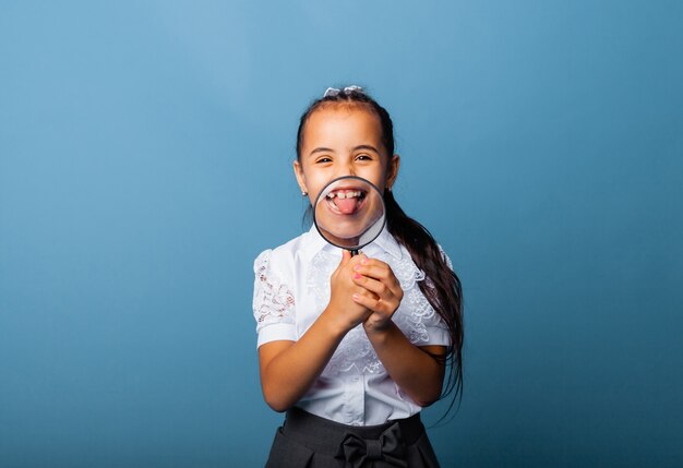 Niña sosteniendo una lupa cerca de su boca y mostrando su lengua sobre un fondo rosa