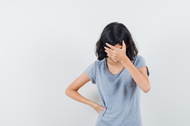 Niña sosteniendo la mano en la cara en camiseta y luciendo deprimida. vista frontal.