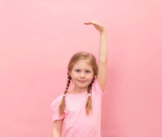 Niña sosteniendo la mano mostrando cuánto más crecerá sobre fondo rosa