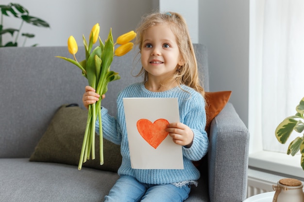 Niña sosteniendo en las manos flores amarillas y postal