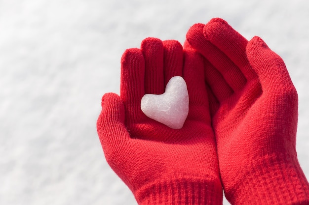 Niña sosteniendo mini corazón de nieve en guantes rojos de lana cálida.