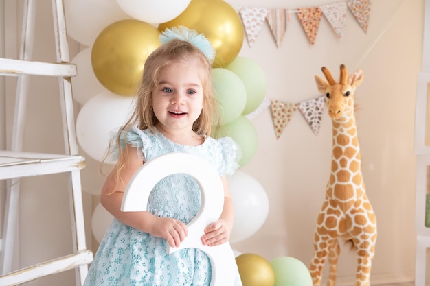 Niña sosteniendo el número 3 en la fiesta de cumpleaños frente al colorido telón de fondo de globos y jirafas