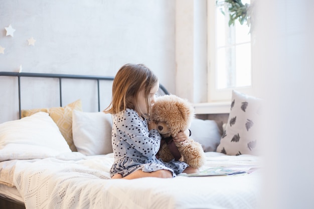 Niña sosteniendo un oso de peluche en la cama en Navidad