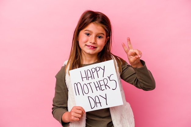 Niña sosteniendo una pancarta del día de las madres felices aislada en la pared rosa