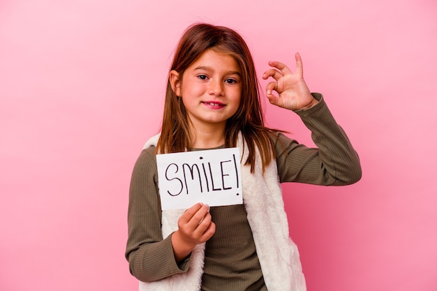 Niña sosteniendo una pancarta de sonrisa sobre fondo rosa