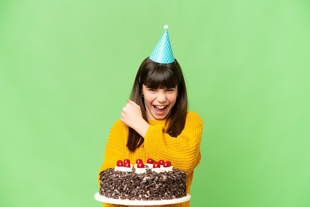 Niña sosteniendo pastel de cumpleaños sobre un fondo clave de croma aislado celebrando una victoria