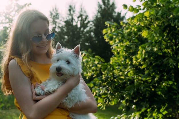 Niña sosteniendo un pequeño perro blanco al sol en el parque