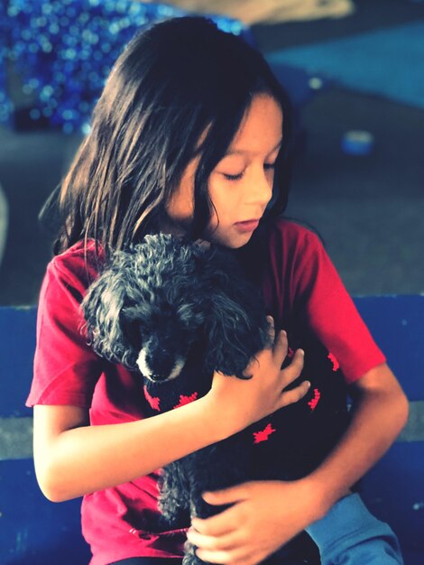 Foto niña sosteniendo un perro mientras está sentada en un banco