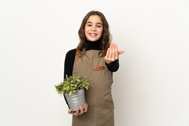 Niña sosteniendo una planta aislada sobre fondo blanco que invita a venir con la mano. Feliz de que hayas venido