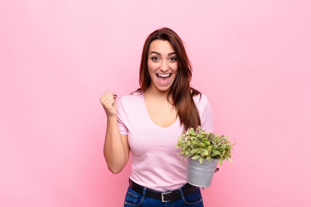 Niña sosteniendo una planta en maceta sonriendo y celebrando