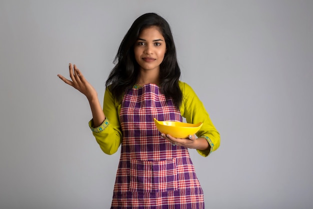 Niña sosteniendo y posando con plato y tazón de utensilios de cocina en un gris